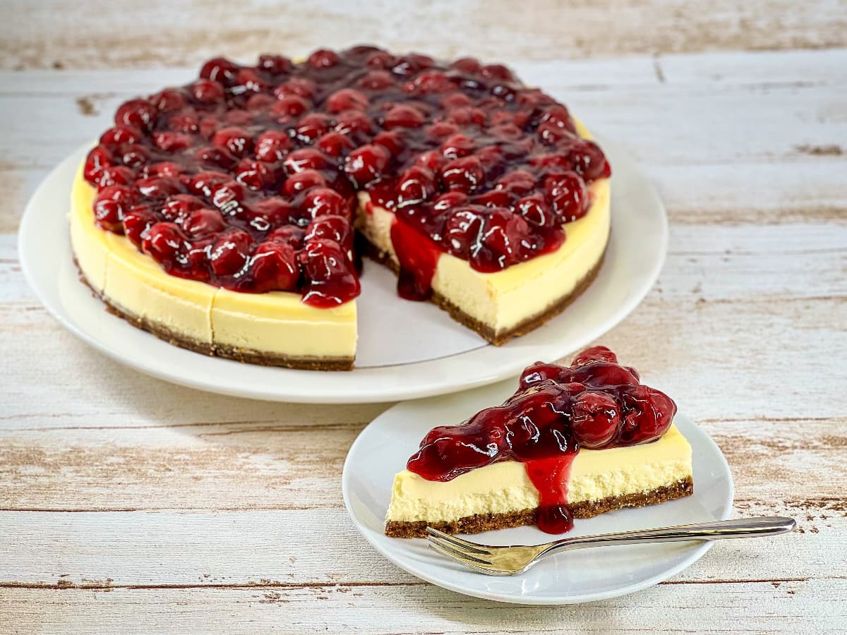 Grote kersen cheesecake met een los puntje ernaast op een schoteltje